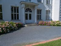 a woman stands outside an upscale building on a sidewalk with flowers in front of the door