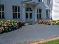 a woman stands outside an upscale building on a sidewalk with flowers in front of the door