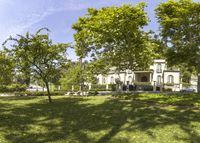 a large house surrounded by lots of green trees in front of some white buildings and blue sky