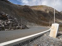 a stone sitting next to the side of a road in a mountainous area near a steep mountain