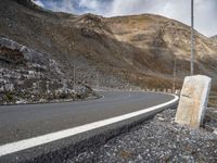 a stone sitting next to the side of a road in a mountainous area near a steep mountain