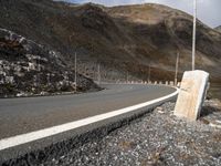 a stone sitting next to the side of a road in a mountainous area near a steep mountain