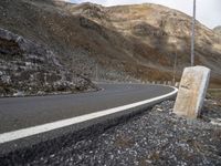 a stone sitting next to the side of a road in a mountainous area near a steep mountain