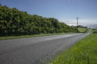 a road next to the side of a green hillside, and power lines and wires