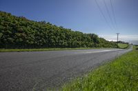 a road next to the side of a green hillside, and power lines and wires