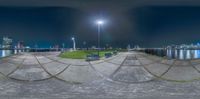 a fisheye photo of a park bench and lights near the water on a clear night