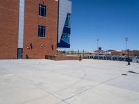 a young man skateboarding across a cement parking lot under blue skies and buildings in front of it