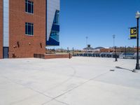 a young man skateboarding across a cement parking lot under blue skies and buildings in front of it