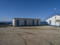 two sheds with their doors open are outside near the ocean, in front of some other wooden buildings