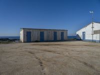 two sheds with their doors open are outside near the ocean, in front of some other wooden buildings