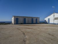 two sheds with their doors open are outside near the ocean, in front of some other wooden buildings