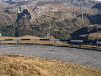 a long train traveling down tracks near mountains on a sunny day with snow capped mountains