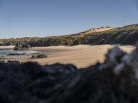 a man walking along a beach towards the water and sand of another beach with a large amount of rocks and mountains