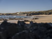 a man walking along a beach towards the water and sand of another beach with a large amount of rocks and mountains