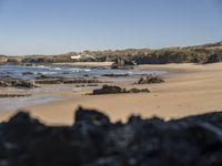 a man walking along a beach towards the water and sand of another beach with a large amount of rocks and mountains