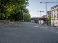 a tree lined road next to a body of water with lots of trees and a building under construction