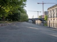 a tree lined road next to a body of water with lots of trees and a building under construction