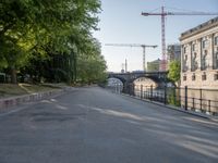 a tree lined road next to a body of water with lots of trees and a building under construction