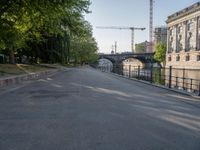 a tree lined road next to a body of water with lots of trees and a building under construction