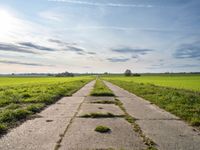 an empty stone pathway in a grassy field and a sky with some clouds above it