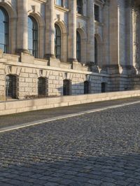 a street with a brick paved road below a big building with pillars and columns around it
