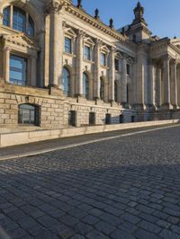 a street with a brick paved road below a big building with pillars and columns around it