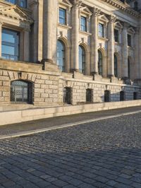 a street with a brick paved road below a big building with pillars and columns around it