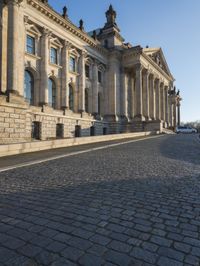 a street with a brick paved road below a big building with pillars and columns around it