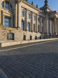 a street with a brick paved road below a big building with pillars and columns around it