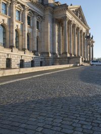 a street with a brick paved road below a big building with pillars and columns around it