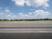 a man riding his motorcycle down an empty road near green grass and shrubs in the background