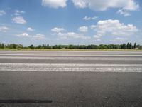 a man riding his motorcycle down an empty road near green grass and shrubs in the background