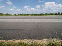 a man riding his motorcycle down an empty road near green grass and shrubs in the background