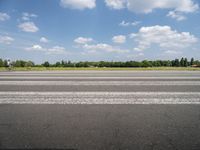 a man riding his motorcycle down an empty road near green grass and shrubs in the background