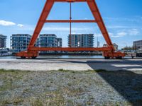 an orange crane on the docks looking out to the water with some buildings behind it