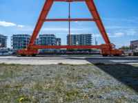 an orange crane on the docks looking out to the water with some buildings behind it