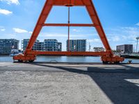 an orange crane on the docks looking out to the water with some buildings behind it