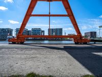 an orange crane on the docks looking out to the water with some buildings behind it