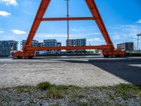 an orange crane on the docks looking out to the water with some buildings behind it