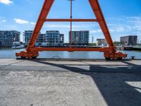 an orange crane on the docks looking out to the water with some buildings behind it