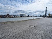 an empty parking area with buildings and water in the background, and a lot of clouds overhead