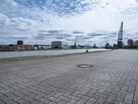 an empty parking area with buildings and water in the background, and a lot of clouds overhead