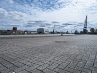 an empty parking area with buildings and water in the background, and a lot of clouds overhead