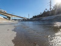 an empty road and street in front of an overpass of a bridge with water going under it