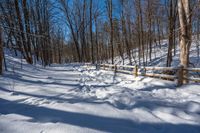 a wooden fence covered in snow near trees and a bench in the background is a forest