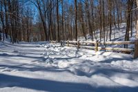 a wooden fence covered in snow near trees and a bench in the background is a forest