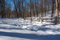 a wooden fence covered in snow near trees and a bench in the background is a forest