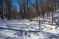 a wooden fence covered in snow near trees and a bench in the background is a forest