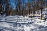 a wooden fence covered in snow near trees and a bench in the background is a forest