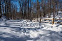 a wooden fence covered in snow near trees and a bench in the background is a forest